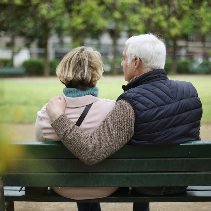 An elderly couple sitting on a public bench in a public garden