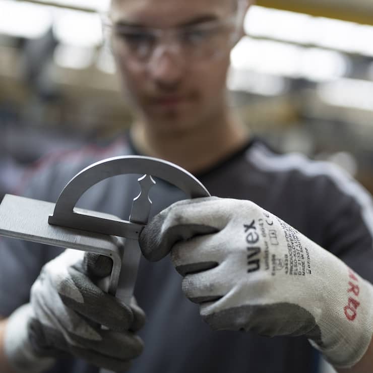Ein Mitarbeiter von Schindler biegt mit der hydraulischen Biegemaschine und misst den Winkel eines Teils eines Schindler Lifts, fotografiert am Donnerstag, 17. Juli 2025 im Hauptsitz von Schindler in Ebikon. (KEYSTONE/Gaetan Bally)