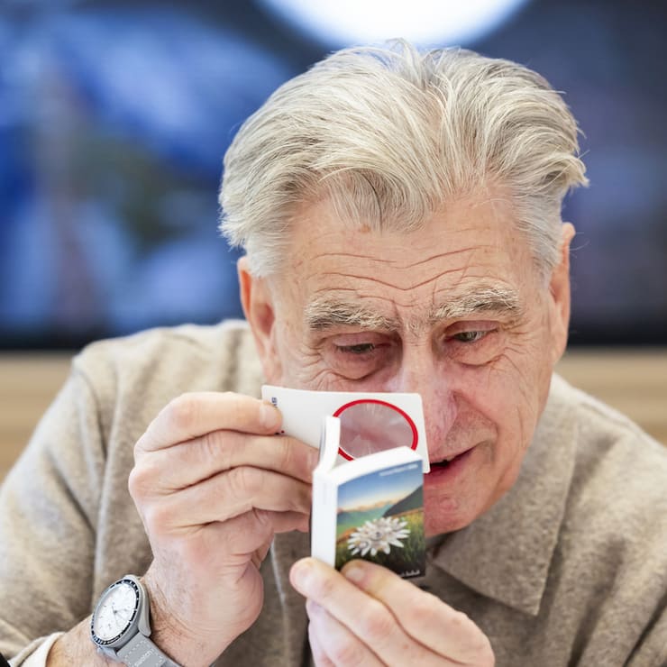 Nick Hayek, CEO Swatch Group AG, looks at the annual report with a magnifying glass, prior to a press conference to present the annual results for 2024, Wednesday, March 19, 2025, in Biel, Switzerland. (KEYSTONE/Peter Klaunzer)