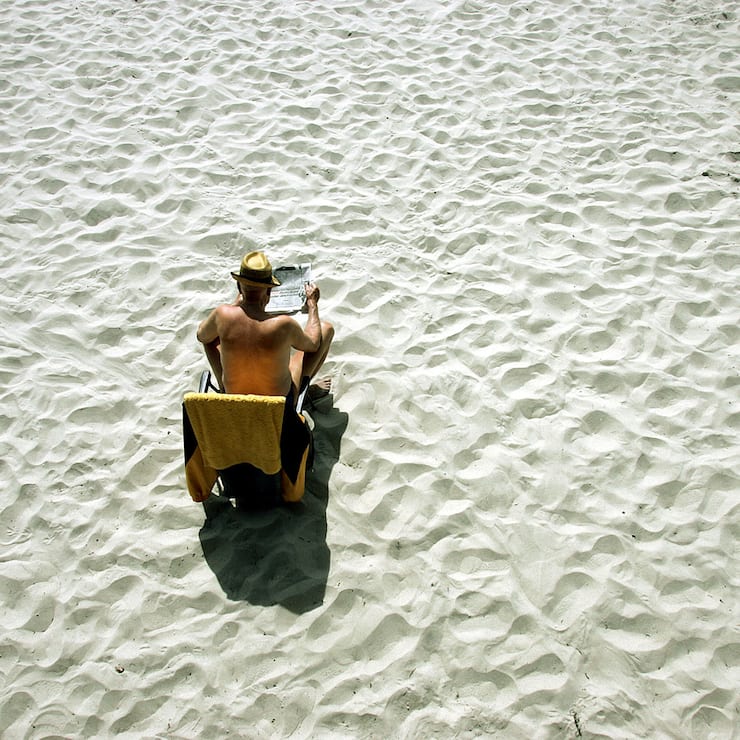 Von viel Sand umgeben sitzt dieser Mann alleine an einem Strand. Luftaufnahme.