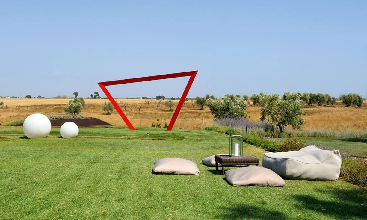 Skulpturenpark: Lounge-Feeling kommt auch im 5000-Quadratmeter-Garten auf – mit Kissen und Tischchen von Paola Lenti und den Lampen Globo von Slide Design. Die Eisenskulptur der Künstlerin Chiara Castria stellt ein Tor dar, welches das Morgenrot einfängt.