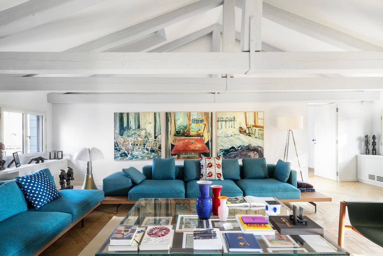 Im Wohnsalon mit den blauenSofas von Piero Lissoni dominiert das Triptychon von SophieWesterlind (o.). Links sieht man ­afrikanische Skulpturen aus der Sammlung von Didier Guillon,auf dem Tisch stehen bunteVenini-Vasen aus Murano. Beider Tischlampe handelt es sichum das Modell Pipistrello von ­Martinelli Luce.