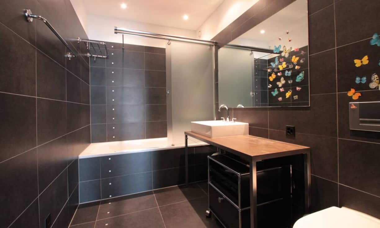 Das grössere der beiden Badezimmer ist mit einer Duschwanne ausgestattet. Grosse, dunkle Keramikplatten an den Wänden und am Boden sorgen für eine gemütliche Atmosphäre.