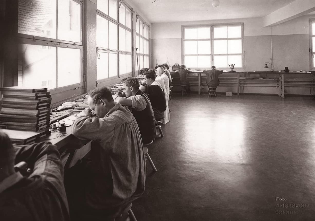 Uhrenmacher arbeiten nebeneinander vor einer Fensterfront in der Felca-Manufaktur, ca. 1920.