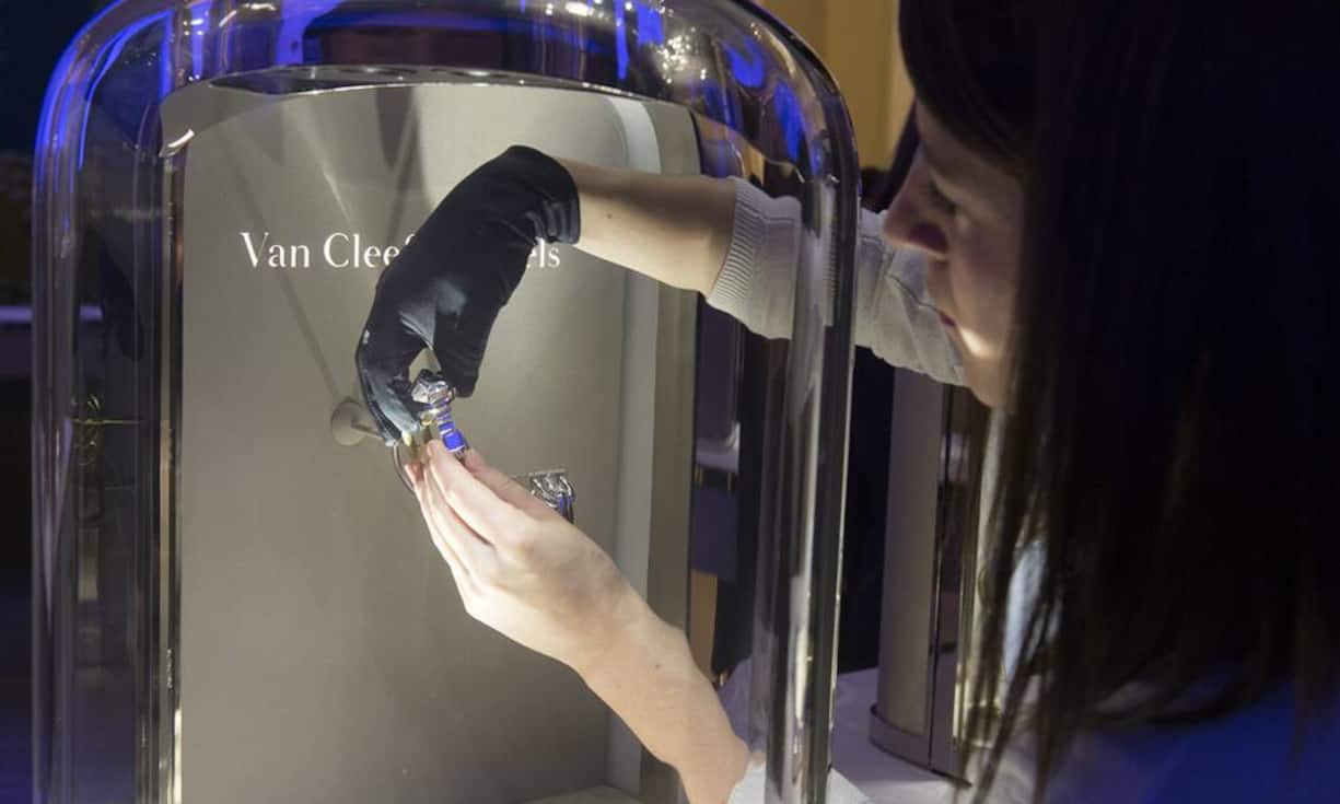 Eine Hostess nimmt vorsichtig eine Uhr von AA Van Cleef & Arpels aus der Vitrine.