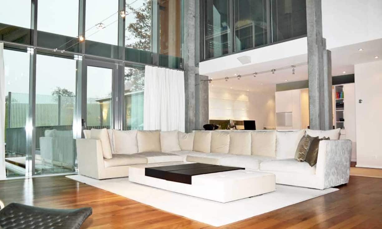 Der Wohn- und Essbereich hat eine imposante Deckenhöhe von über sieben Metern. Bodentiefe Fenster sorgen für Lichtdurchflutung und helle Räume. Im Wohnzimmer findet sich ein Cheminée sowie ein offener Arbeitsbereich.