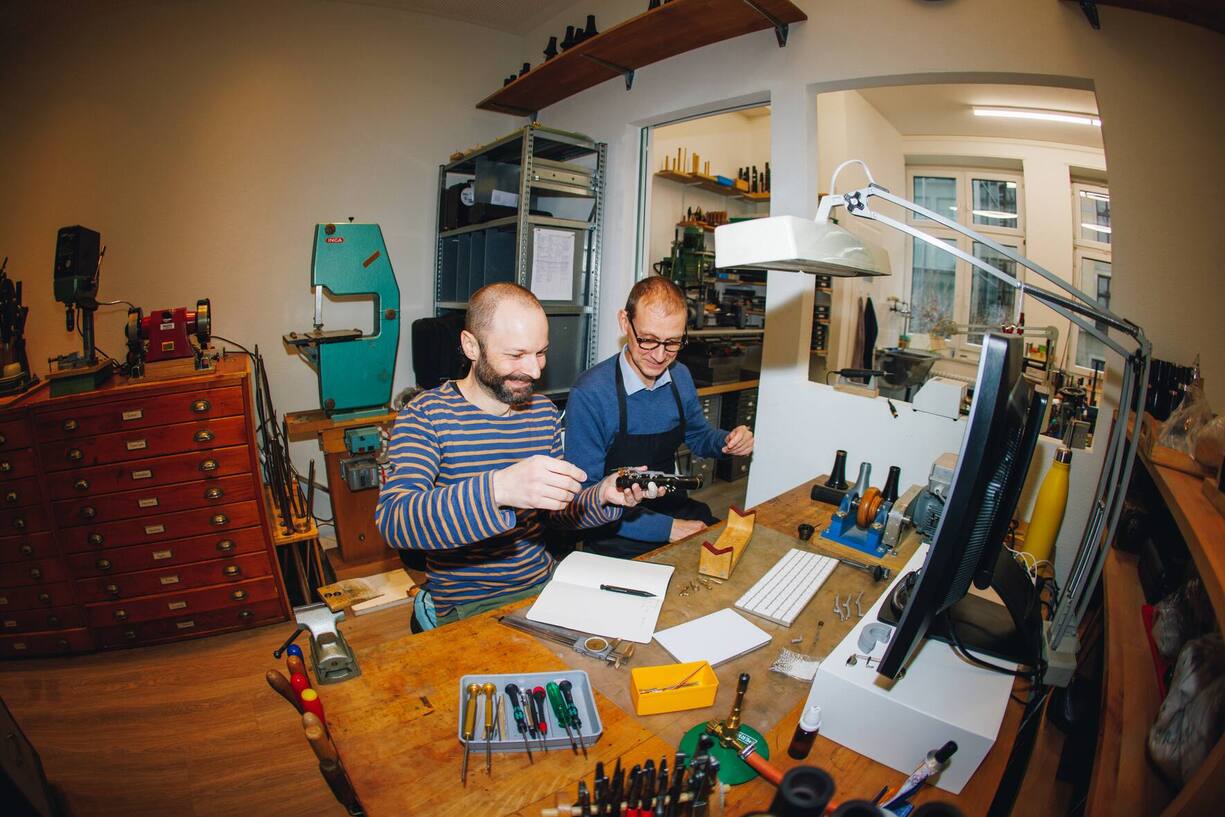 Zwei Instrumentenbauer sitzen an einem Tisch in der Werkstatt und werkeln an einem Klarinettenstück.