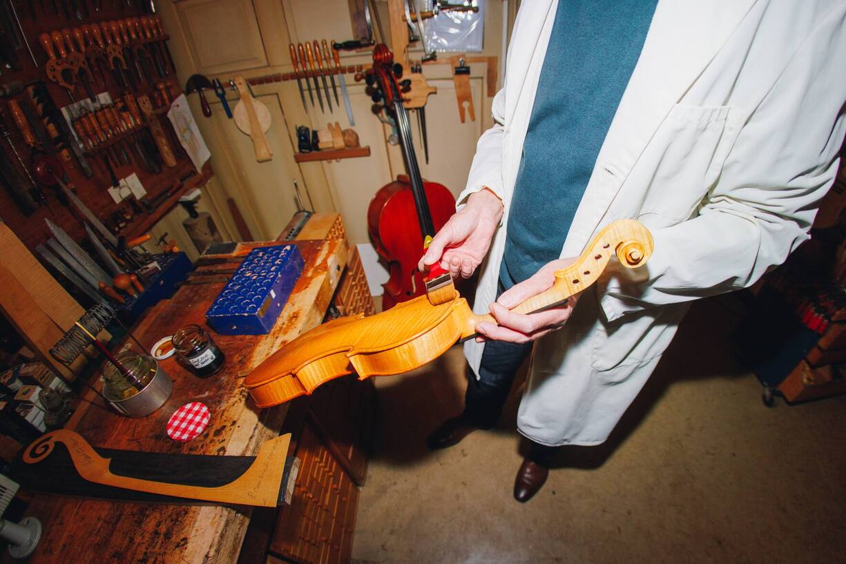 Der Geigenbauer hält eine Rohversion einer Geige in der Hand.