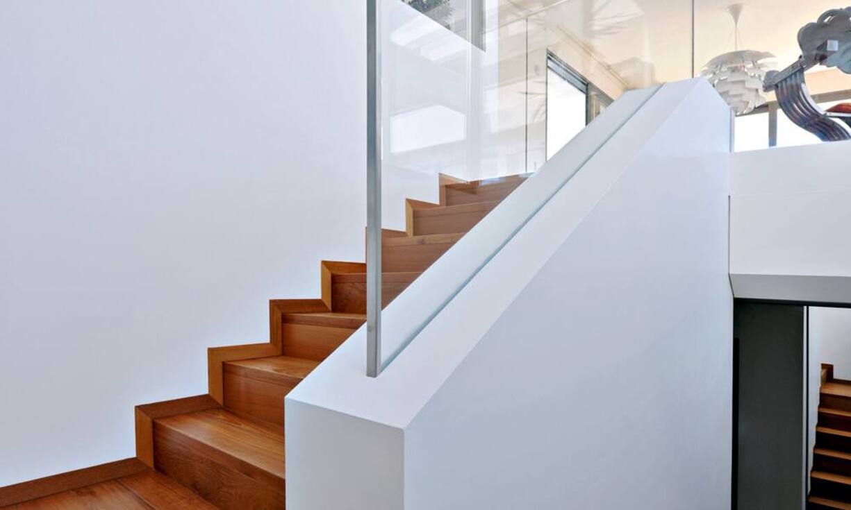 Aufstieg: Die Treppe, die vom Haupteingang nach oben direkt in den Wohnraum führt, liegt im hinteren Bereich des Hauses, an der Hangseite. Sie erhält ihr natürliches Licht aus dem Patio. Links oben sieht man die Glaswand der Küche.