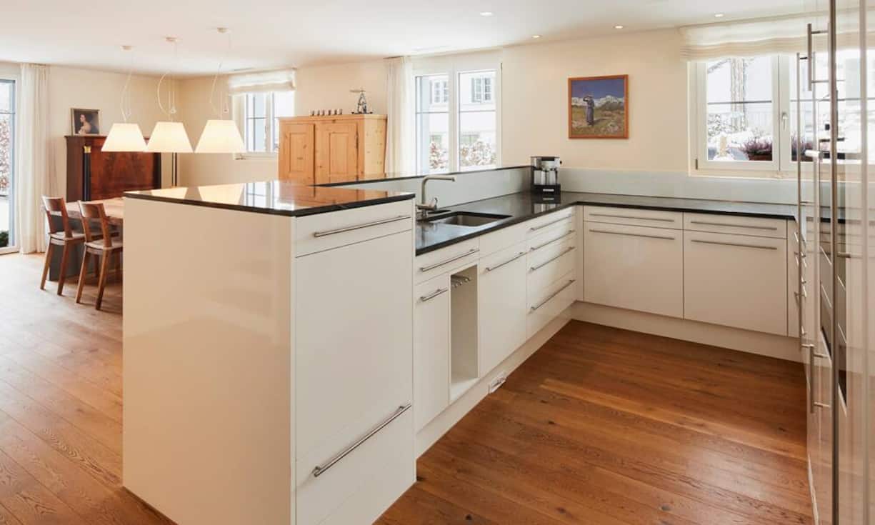 Vom Eingangsbereich wird man in die helle Küche gelockt. Sie bietet einen hohen Ausbaustandard mit grosszügiger, erhöhter Arbeitsfläche aus einem dunklen Granit, einem Kombisteamer sowie einem Geschirrspüler.