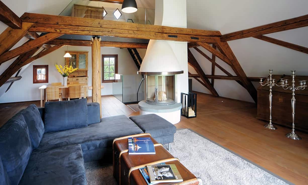 Der Dachtsock wurde bis zum Giebel ausgebaut und kommt dadurch luftig daher. Die originalen Holzbalken und das Cheminee mitten im Raum geben dem Wohnzimmer eine gemütliche Atmosphäre.