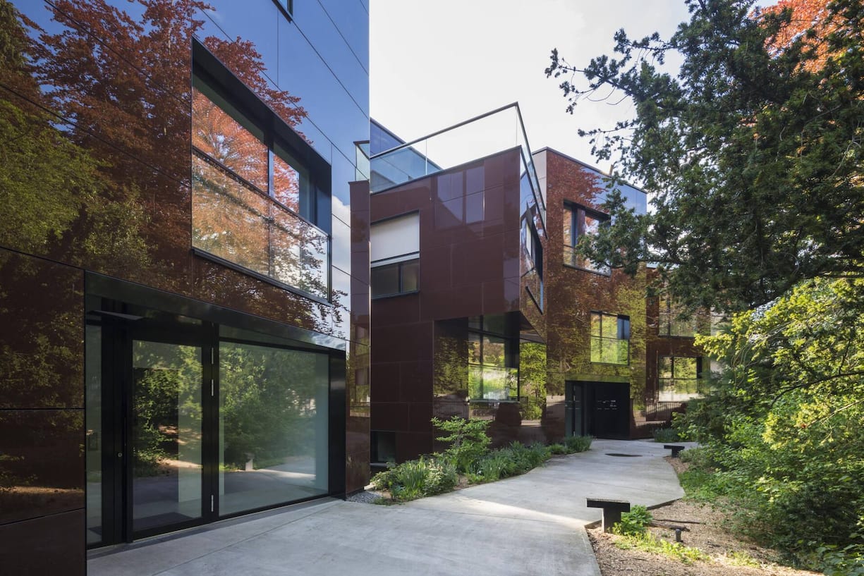 Wohnhäuser Zollikerstrasse in Zürich. Dunkelbraun emaillierte Glasplatten an der Fassade spiegeln die alten Buchen, Kiefern und Mammutbäume.