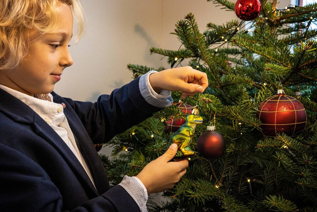 Kind hält Weihnachtsbaumschmuck in Dinosaurierform in den Händen.