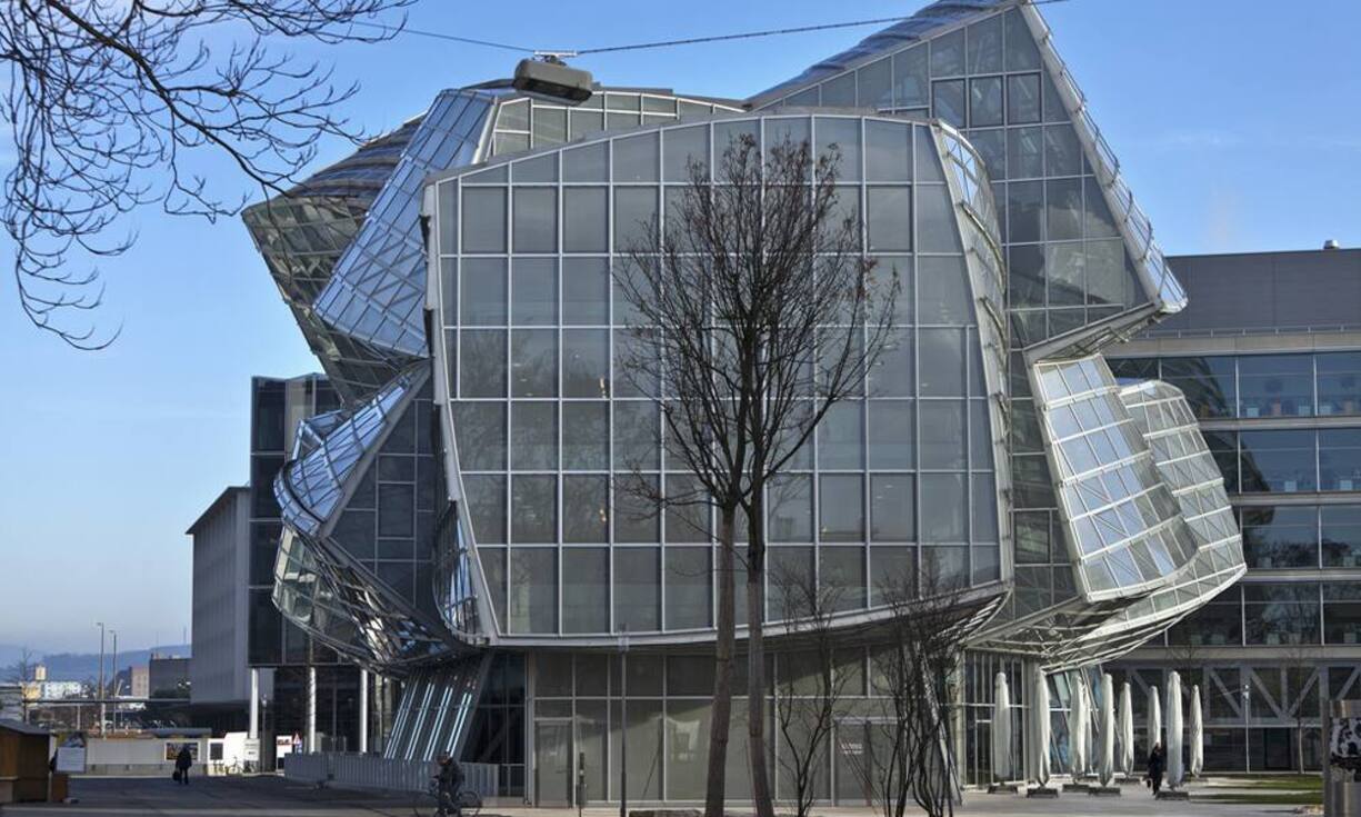 Novartis-Campus, Basel, Frank Gehry, 2009: Auf dem Novartis-Campus in Basel zeigen die Weltmeister der Architektur ihre Muskeln und lehren uns, wie ein Meisterstück neben dem andern brillanten Soli, jedoch kein Konzert macht - im Bild das heiter schiefe Glashaus von Frank Gehry.