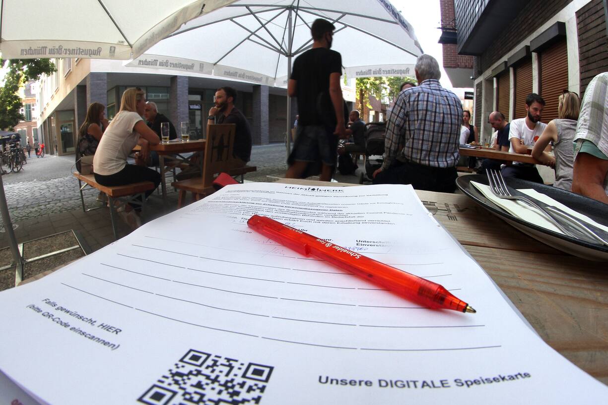 Kontaktbogen zur Erfassung persönlicher Daten für eine mögliche Nachverfolgung von Kontaktketten liegt mit desinfiziertem Kugelschreiber und Besteck auf einem Tisch im Außenbereich einer Gaststätte in der Innenstadt von Düsseldorf