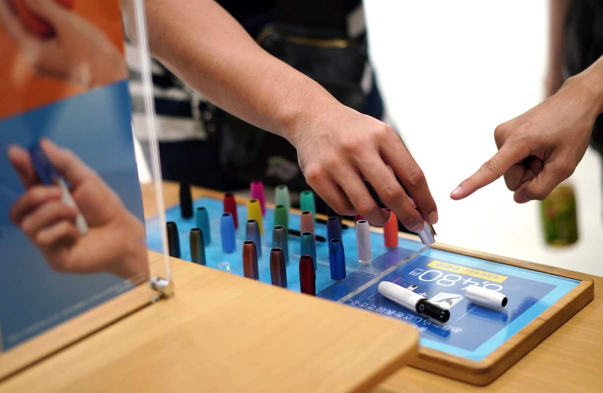 In this Oct. 22, 2018 photo, visitors look at a pen-like "heat-not-burn" device iQOS at an IQOS store in Tokyo. In Japan, Philip Morris opened nine iQOS stores in trendy districts nationwide, offering free WiFi and drinks, to perk consumer interest. (AP Photo/Eugene Hoshiko)