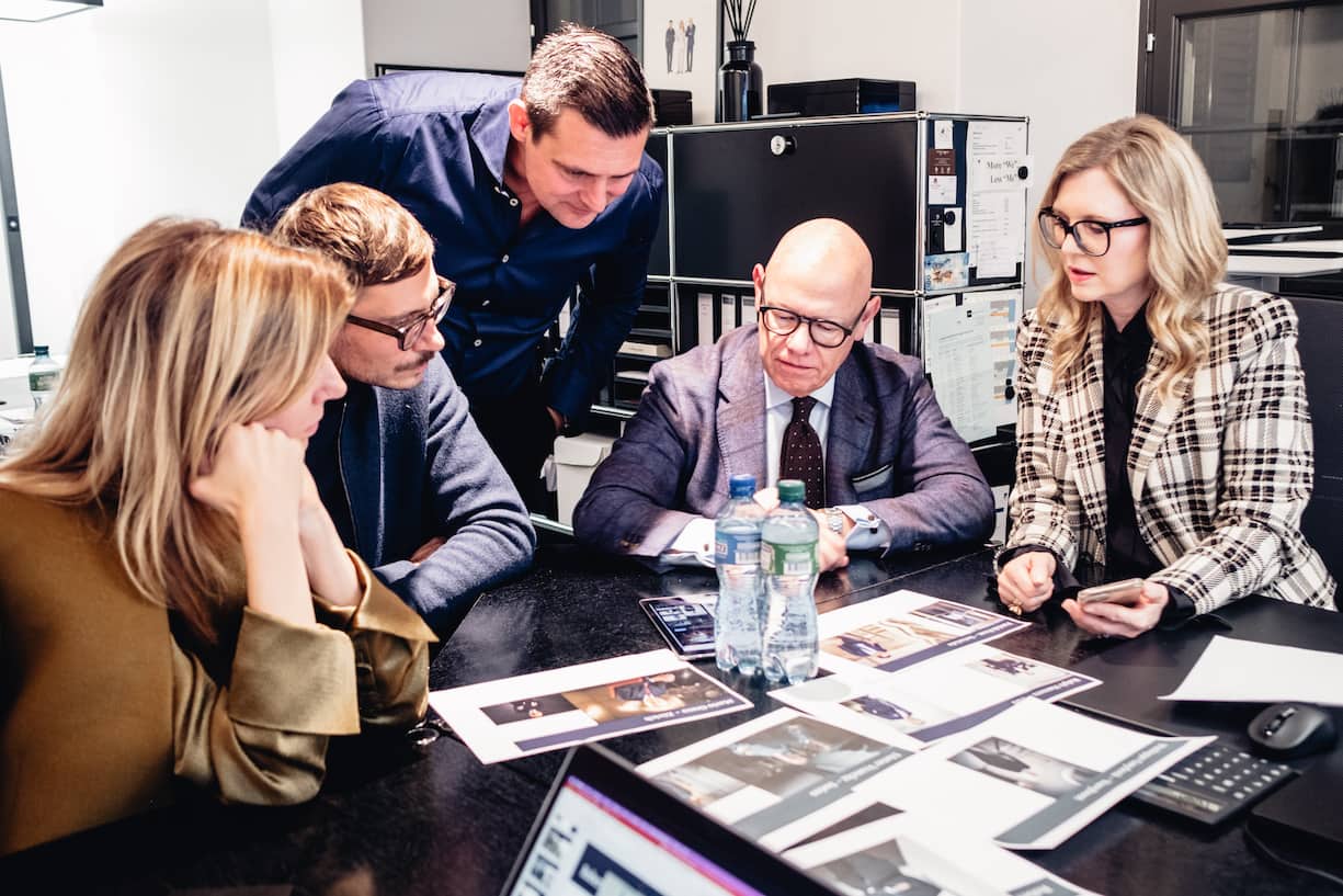 Drei Männer und zwei Frauen sitzen an einem Tisch und besprechen anhand von Fotos den Stil der Chefs.