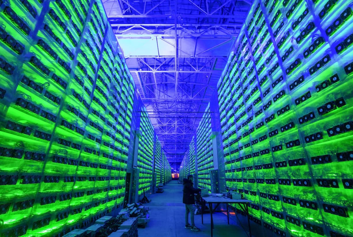 A worker inspects hardware devices as illuminated mining rigs operate inside racks at the CryptoUniverse cryptocurrency mining farm in Nadvoitsy, Russia, on Thursday, March 18, 2021. The rise of Bitcoin and other cryptocurrencies has prompted the greatest push yet among central banks to develop their own digital currencies. Photographer: Andrey Rudakov/Bloomberg