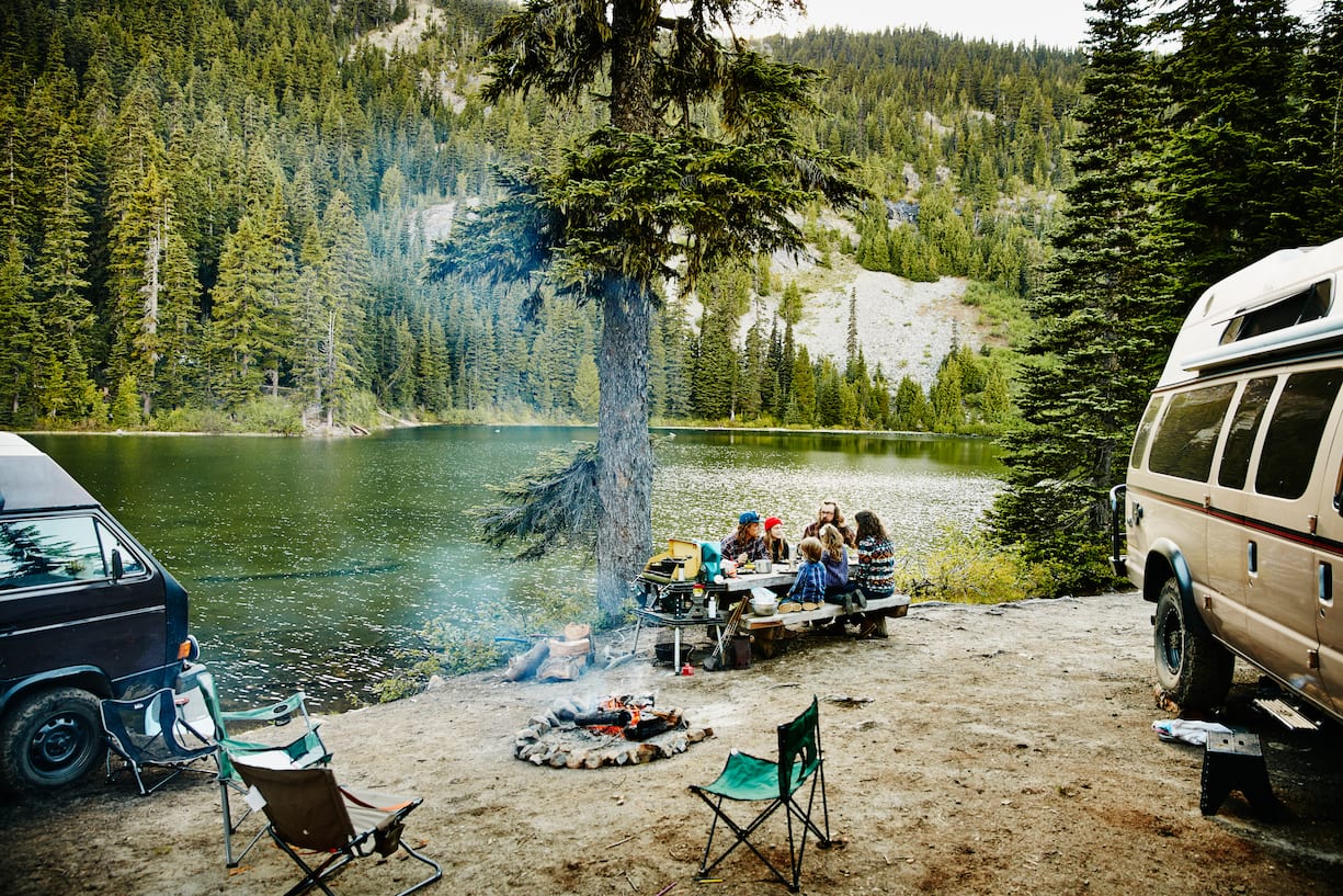 Family and friends sharing a meal together at campsite by lake in mountains