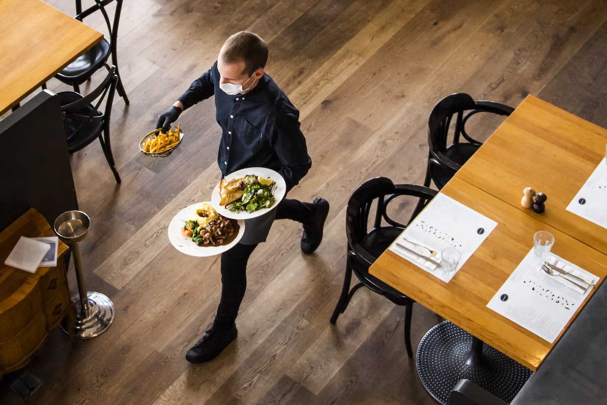 A waiter of "La Brasserie de Montbenon" restaurant brings dishes food to customers during the spread of the pandemic Coronavirus (COVID-19) disease in Lausanne, Switzerland, Monday, May 11, 2020. In Switzerland from today, the Swiss authorities lifted second part of the lockdown. (KEYSTONE/Jean-Christophe Bott)