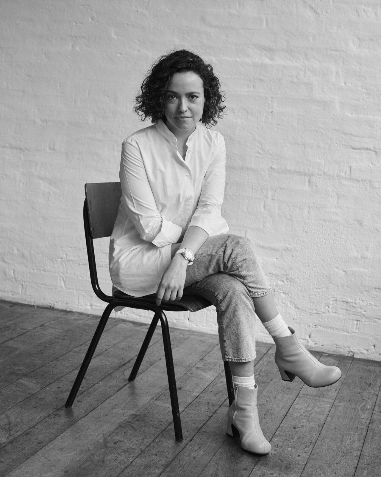 Schwarz-Weiss-Bild von Aurelia Figueroa auf einem Stuhl sitzend.