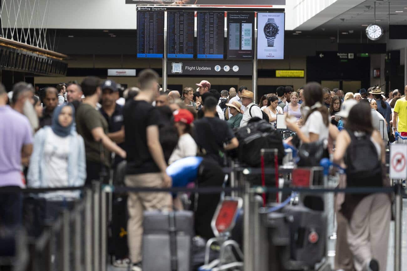 Passengers look at screens informing them of the flight situation, on Friday, 19 July 2024, at the airport Zurich in Kloten, Switzerland. Due to a worldwide IT breakdown, check-in for air travellers and flight operations are severely restricted and most flights are delayed or cancelled. Swiss air traffic control Skyguide is also affected by the IT disruption and has reduced the capacity of Swiss transit traffic as an immediate precautionary measure. (KEYSTONE/Gaetan Bally)