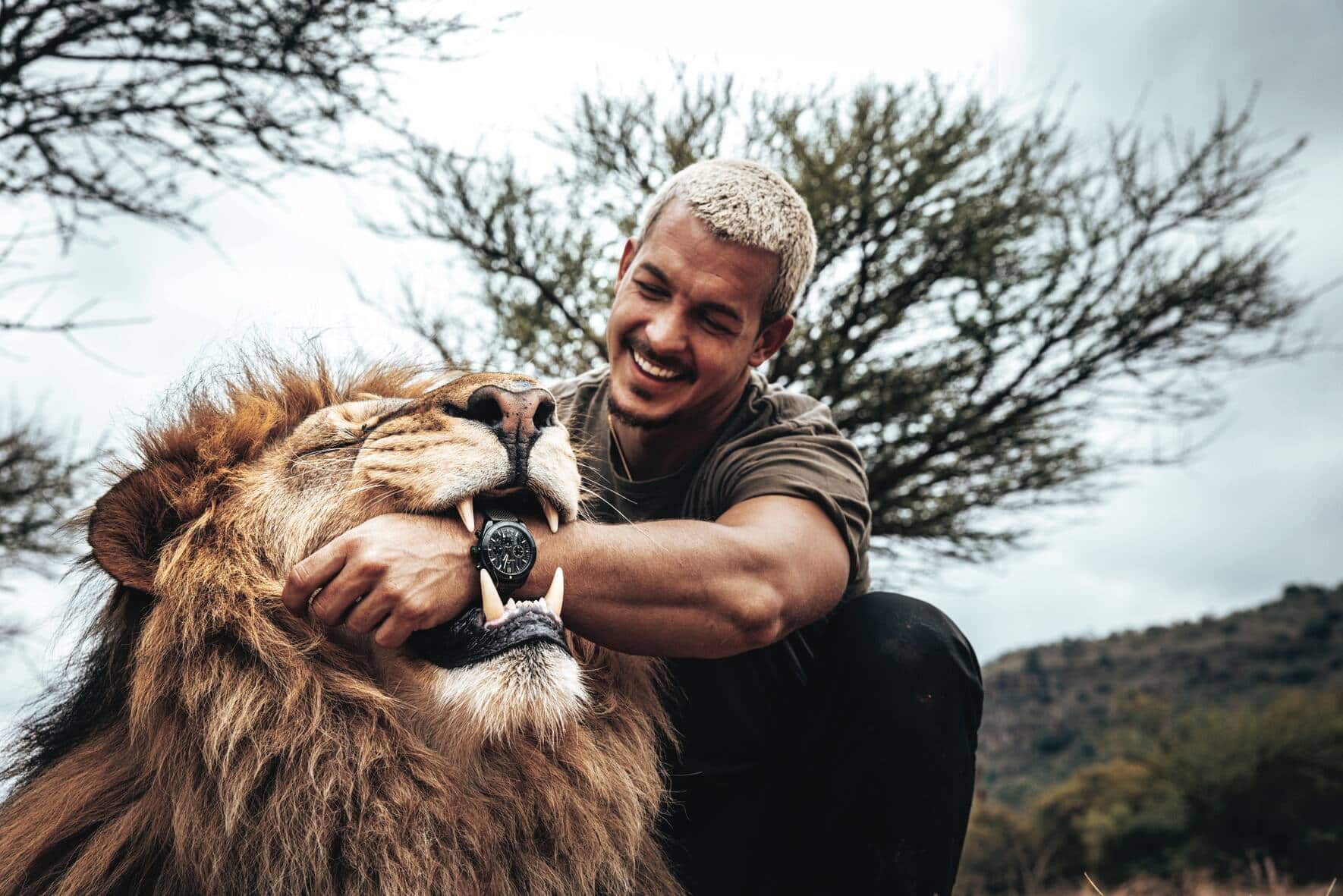 Dean Schneider mit der Norqain-Uhr am Handgelenk und seinem Löwen nebenan.