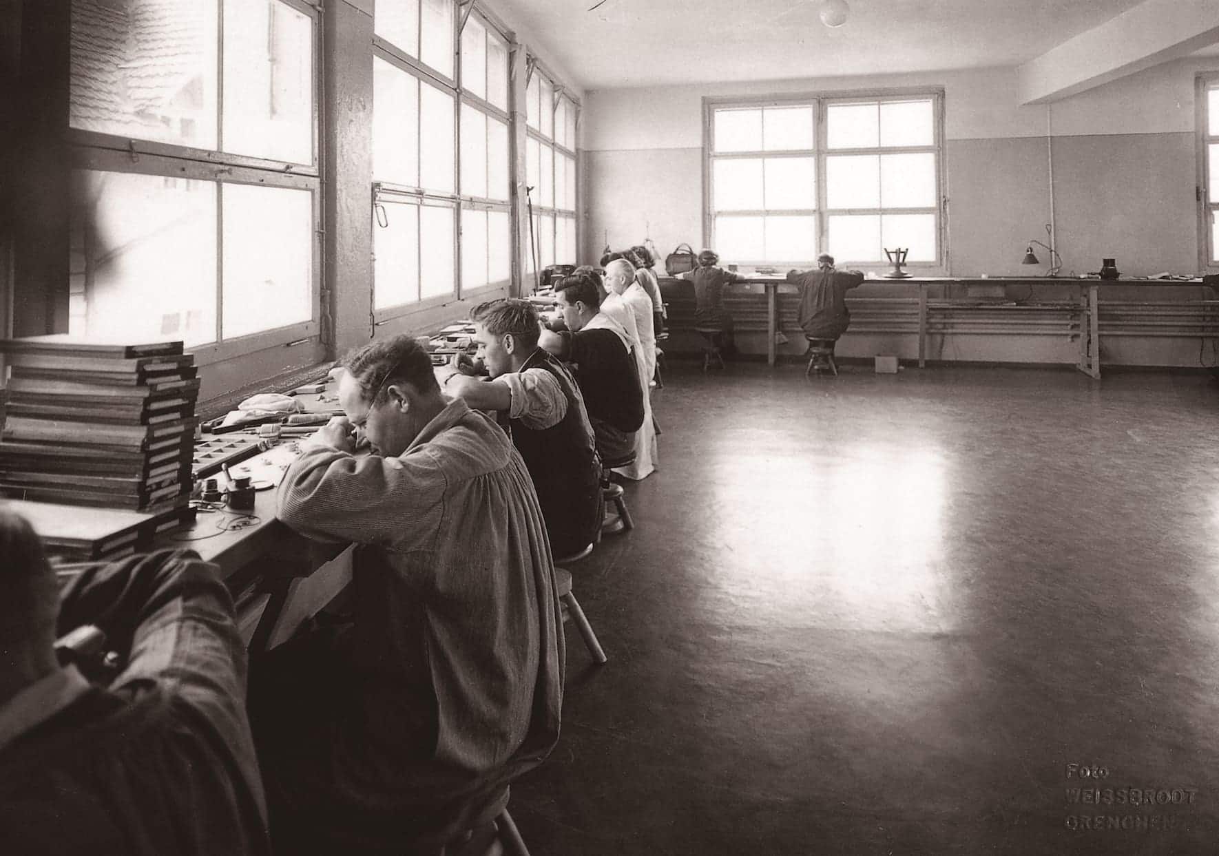 Uhrenmacher arbeiten nebeneinander vor einer Fensterfront in der Felca-Manufaktur, ca. 1920.