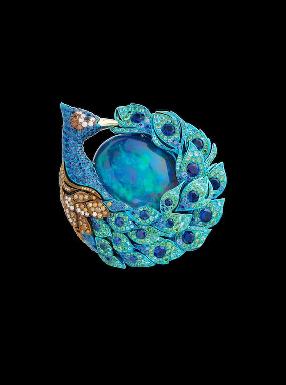 Ein Pfau umschliesst mit seinem schillernden Schweif – vollständig mit Farbsteinen ausgefasst – einen prachtvollen Opal.