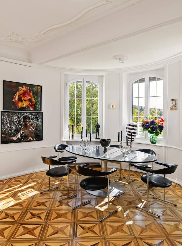 Das Esszimmer bietet reizvolle Ausblicke ins Grüne und besticht durch historische Elemente wie Stuck und Intarsienparkett. Der Esstisch setzt sich aus einem Fuss von Knoll und einer massgefertigten Platte vom Schreiner zusammen. Die Stühle stammen aus einem Vintage-Laden.