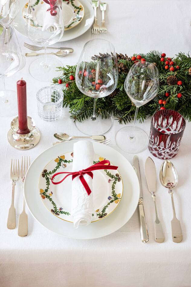 Weihnachtlich gedeckter Tisch mit Porzellangeschirr, Silberbesteck, Weingläsern, Tannenzweigen und Kerzen.