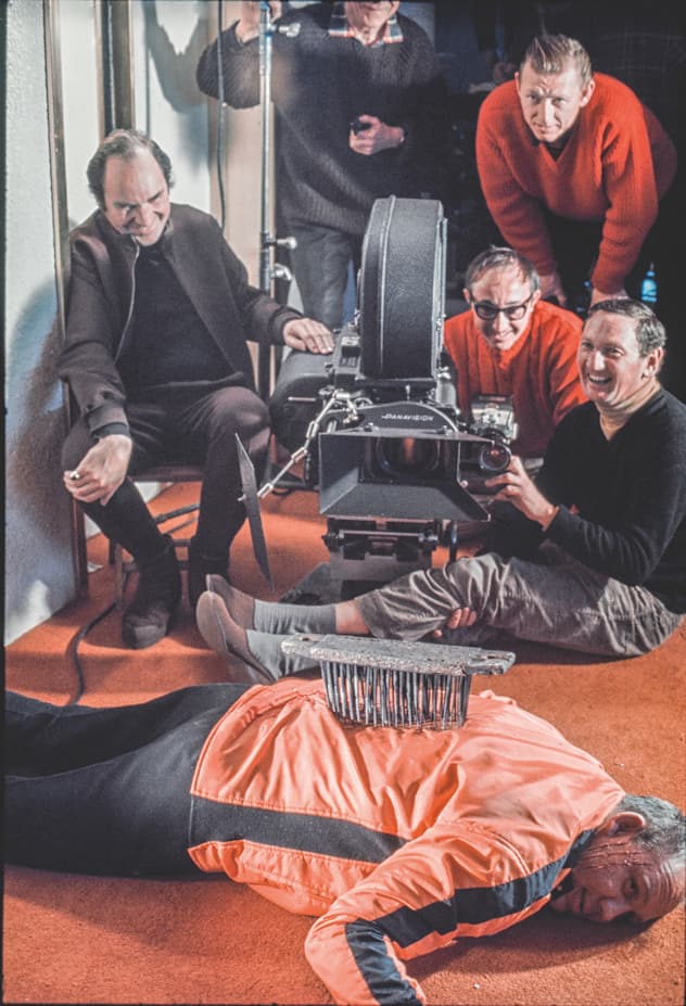 <p>Regisseur Peter Hunt (auf dem Stuhl) amüsiert sich über Bösewicht Yuri Borienko (auf dem Boden liegend).</p>