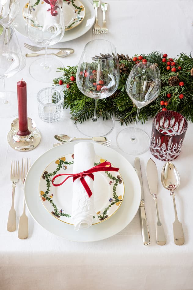 Weihnachtlich gedeckter Tisch mit Porzellangeschirr, Silberbesteck, Weingläsern, Tannenzweigen und Kerzen.