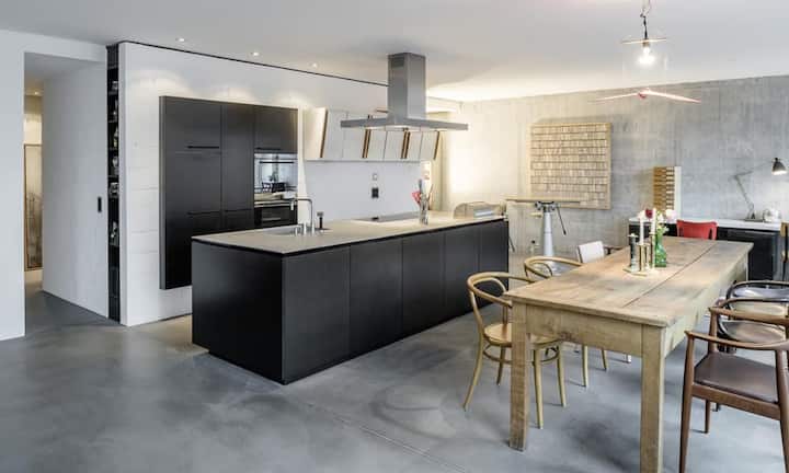 Eine Schreiner-Küche mit Kochinsel lädt zum Kochen ein. Wände aus Sichtbeton sorgen für eine moderne Atmosphäre.