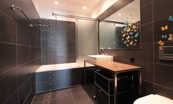 Das grössere der beiden Badezimmer ist mit einer Duschwanne ausgestattet. Grosse, dunkle Keramikplatten an den Wänden und am Boden sorgen für eine gemütliche Atmosphäre.