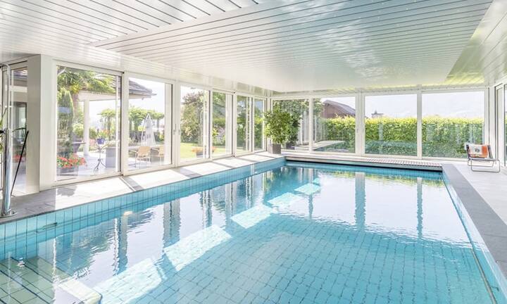 Direkt vom Wohnzimmer gelangt man zum verglasten Anbau mit Innenschwimmbad. Die grossen Schiebetüren auf drei Seiten ermöglichen den Gang zum Garten.