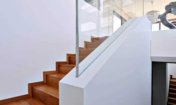 Aufstieg: Die Treppe, die vom Haupteingang nach oben direkt in den Wohnraum führt, liegt im hinteren Bereich des Hauses, an der Hangseite. Sie erhält ihr natürliches Licht aus dem Patio. Links oben sieht man die Glaswand der Küche.