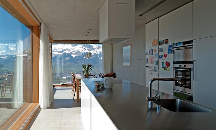 Auf 786 Metern, oft über dem Nebelmeer, liegt der Neubau im Dorf Planken. Vom offenen Küchen-Ess-Bereich wie vom Home Office unter demselben Dach sieht man durch grosse Panoramascheiben auf die Schweizer Berge.