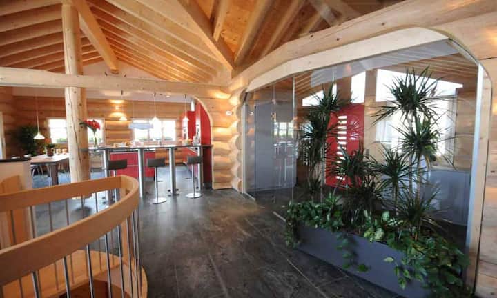 Die Atmosphäre im Wohnhaus ist geprägt von hochwertigen Steinplatten und dem verwendeten Holz der Weisstanne. Rote Farbtupfer wie beispielsweise in der Küche setzen Akzente. Auf insgesamt drei Etagen und 403 Qadratmetern Bruttowohnfläche verteilen sich 8 Zimmer.