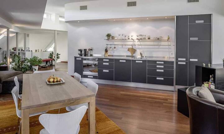 Der offene Wohn-/Essbereich mit Bulthaup-Küche und Edelstahlabdeckung verfügt über ein Cheminée.