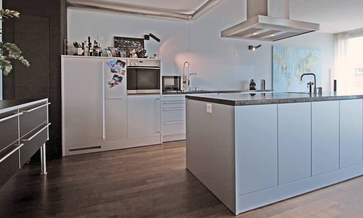 Die Bulthaup Küche mit Küchengeräten von Miele verfügt über eine grosse Kochinsel mit viel Arbeits- und Staufläche. Die Küche öffnet sich zum grossen Wohn-Essbereich hin.