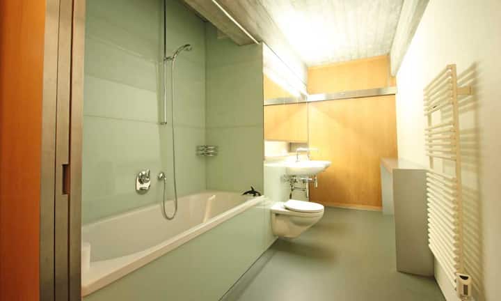 Zwischen den Zimmern platziert ist das grosse Badezimmer mit zwei Waschtischen, Dusch-/Badewanne und angrenzender begehbarer Ankleide.