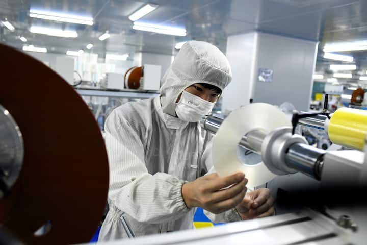DONGGUAN, CHINA - MAY 20: Employees wearing protective suits work on the production line of optical film products at a workshop of Guangzhi Photoelectric Co., Ltd on May 20, 2020 in Dongguan, Guangdong Province of China. (Photo by Zhan Youbing/VCG via Getty Images)