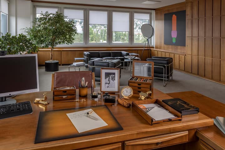 Schreibtisch mit diversen Schreibutensilien: Tintenfässer, Brieföffner, vergoldeter Locher, Schreibunterlage, Köcher aus Leder und ein Fotorahmen mit Bild eines Mannes in den Bergen.