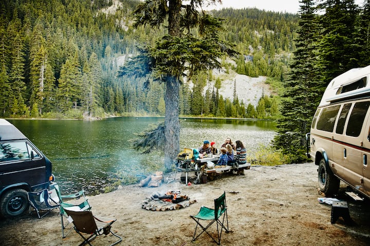 Family and friends sharing a meal together at campsite by lake in mountains