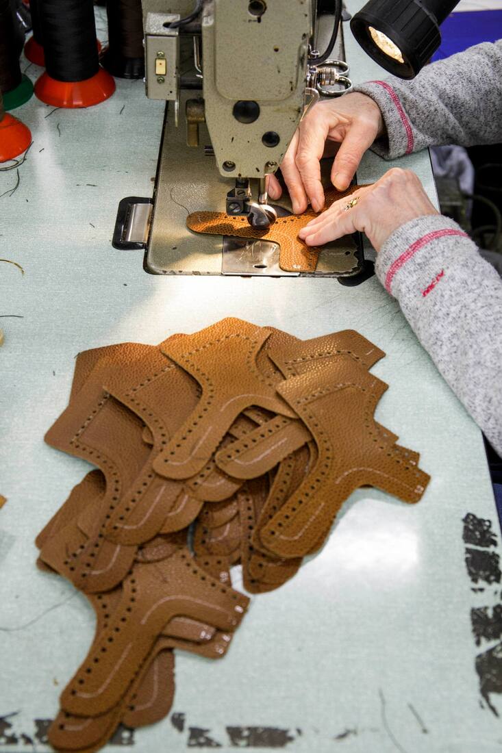 Einzelne Lederteile für Schuhe neben einer Näherin