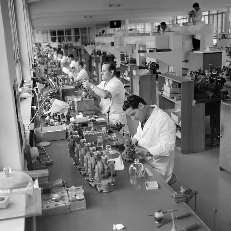 Mitarbeiter der Firma Wild Heerbrugg AG, Hersteller optischer Vermessungsinstrumente, Labor- und Stereo-Mikroskopen, Reisszeugen und Instrumenten fuer die Photogrammetrie, aufgenommen im Kanton St.Gallen am 9. November 1960. Die von der Montage vormontierten Wild-Theodolithen (vorne T16, hinten T29) werden von den Justierern in 10er-Serien fertig justiert. (KEYSTONE/PHOTOPRESS-ARCHIV/Vogt)